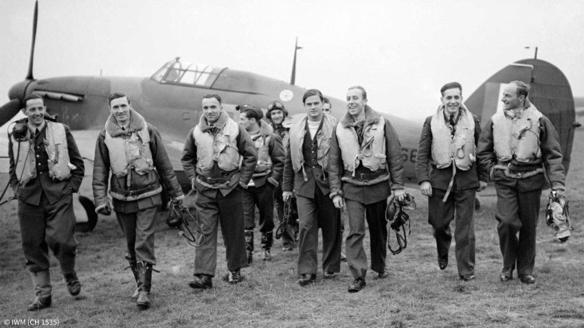 Pilots of No. 303 (Polish) Squadron RAF with one of their Hawker Hurricane fighter aircraft in the backgound, October 1940. The men are walking in a line from left-to-right, towards the camera, many of whom are smiling. Photographs are a valuable source for researching military ancestors, and in this instance, when researching Polish pilots. ©IWM (Ch 1535)