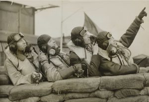 Airmen from Czechoslovakia, serving with the RAF, 1940. The four airmen are leaning on sandbags with the airman and the front pointing at something in the sky; they all gaze skywards. 