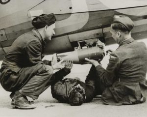 Three members of RAF groundcrew fix a smoke float to a Lysander aircraft in May 1942. One man lays underneath the smoke float to secure it while the other two hold each end of the float. The image caption offers another use of smoke floats: to screen rescue work from possible enemy craft. © Hulton Archive/Getty Images