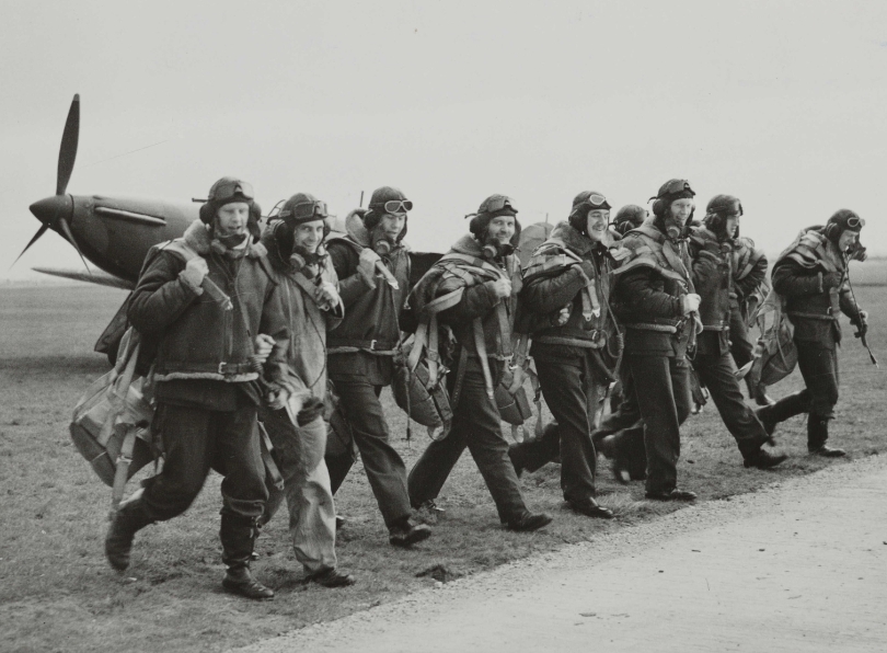 The image shows a group of Canadian pilots during the Battle of Britain in 1940. The group is walking horizontally on an airstrip, turning their heads slightly to look at the camera. A fighter aircraft, possibly a Spitfire, is obscured behind the group. There are many collections on Forces War Records containing Royal Canadian Air Force records or relating to the Canadian air services. ©Hulton Archive/Getty Images