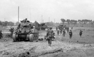 Infantry of the 3rd Division move inland from Sword Beach, past a Sherman Tank of the 27th Armoured Brigade. In the background, M10 3-Inch self-propelled Guns Can be seen. © IWM (B 5080)