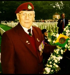 George Matthews later in life at Arnhem Oosterbeek War Cemetery. The image shows George wearing a maroon blazer and beret featuring the badge of the Reconnaissance Corps. George is also wearing his medals and is holding a wreath. In the background are the graves of the fallen, many of whom lost their lives during the Battle of Arnhem. Image courtesy of Gina Matthews. 