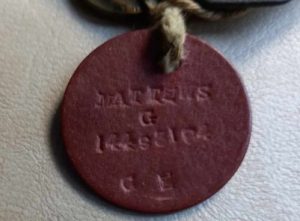 ID Disc, or 'Dog Tags', belonging to Battle of Arnhem veteran George Matthews. The tag is round, dark brown in colour and made of compressed fibre. It is stamped with the service person's name, number and religion. Image courtesy of Gina Matthews.