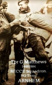 George Matthews, training with the airborne forces in the lead-up to the Battle of Arnhem. The image shows George in uniform, leaning forward as a comrade adjusts his gear. He appears to be wearing a parachute and is smiling, surrounded by smiling comrades. Image courtesy of Gina Matthews. 